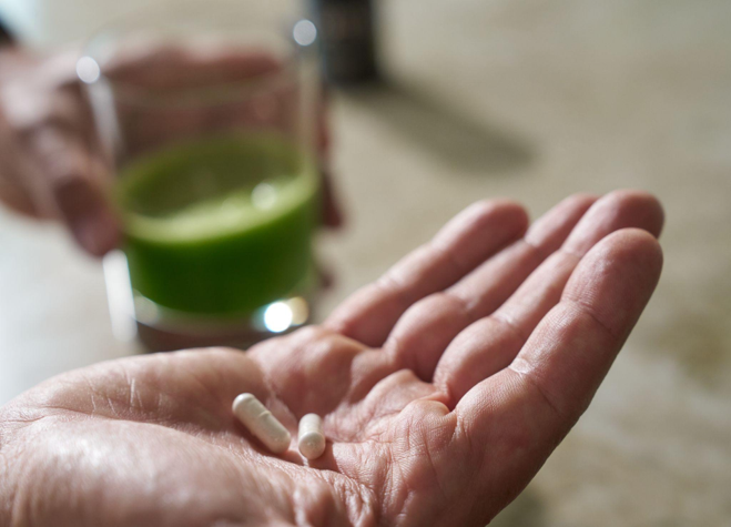 Two aloe capsules in a hand beside an aloe drink